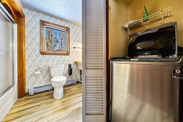 bathroom with a textured ceiling, hardwood / wood-style floors, a baseboard radiator, and toilet