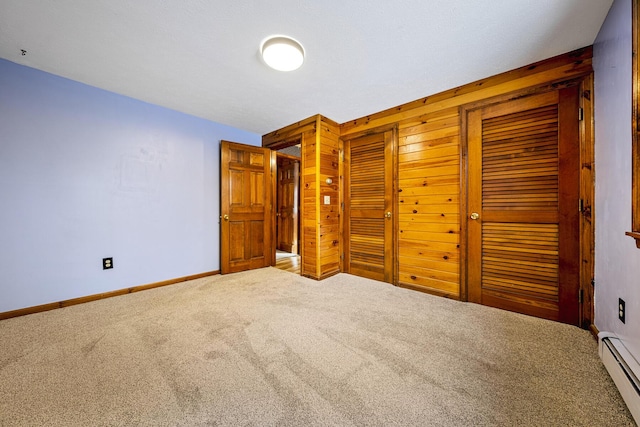 unfurnished bedroom with a baseboard heating unit, carpet floors, and wooden walls