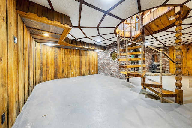 basement featuring brick wall, wood walls, and a wood stove