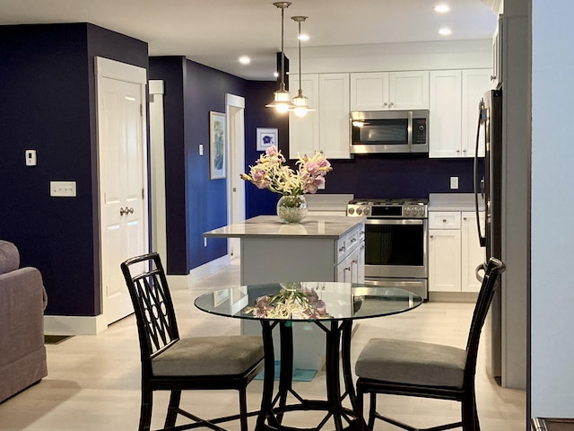 kitchen featuring appliances with stainless steel finishes, white cabinets, decorative light fixtures, and a center island