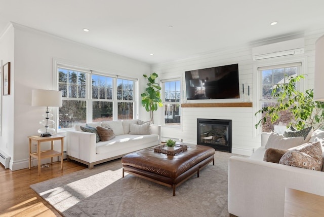 living room with crown molding, a fireplace, a wall mounted AC, and light wood-type flooring