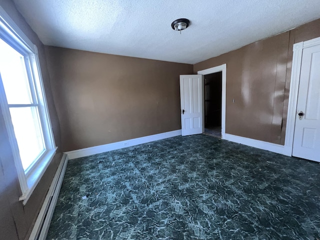 unfurnished room featuring a baseboard heating unit and a textured ceiling