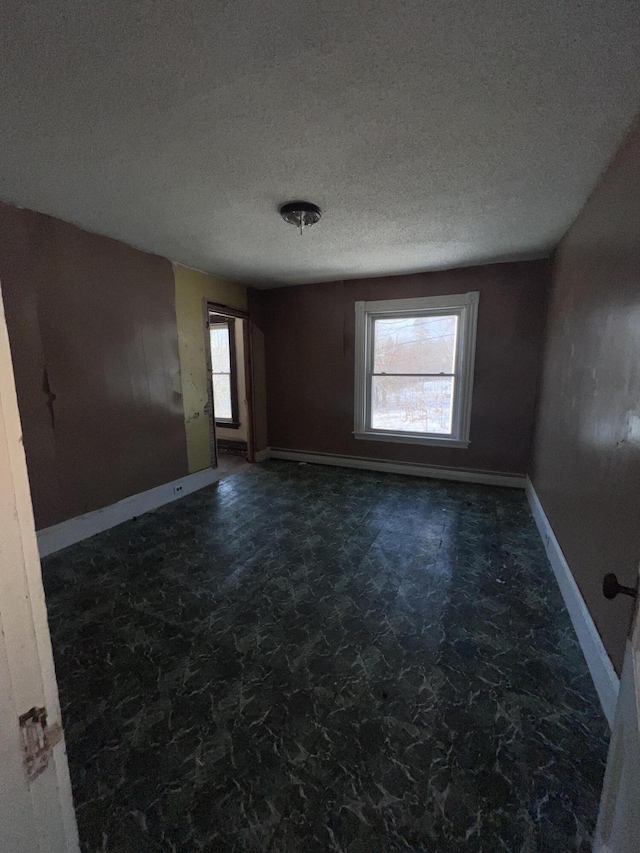 empty room with a textured ceiling, baseboard heating, and plenty of natural light