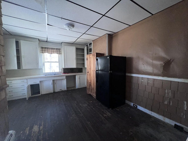 kitchen featuring a drop ceiling, sink, black refrigerator, white cabinets, and dark hardwood / wood-style flooring