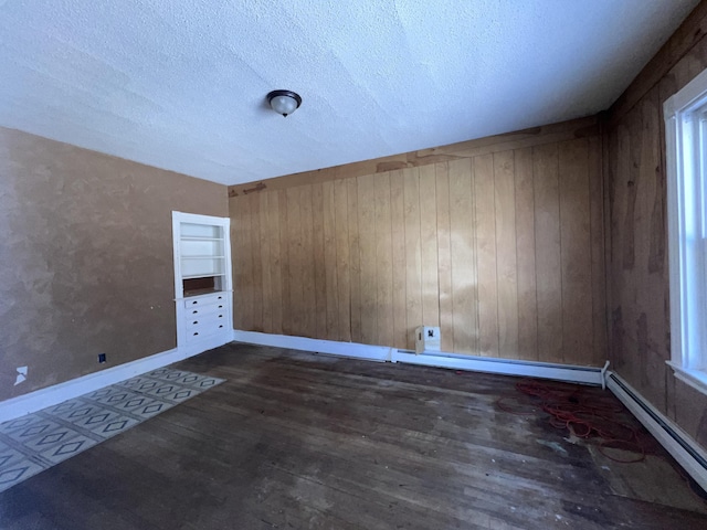 spare room featuring baseboard heating, a textured ceiling, dark wood-type flooring, built in shelves, and wood walls