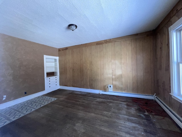 unfurnished room with built in shelves, a baseboard heating unit, wood walls, and a textured ceiling