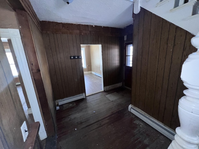 interior space featuring baseboard heating, dark wood-type flooring, wood walls, and a textured ceiling