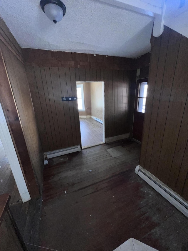 interior space featuring dark wood-type flooring, baseboard heating, a textured ceiling, and wood walls