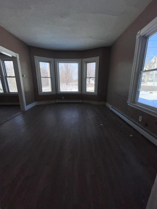 unfurnished room with a textured ceiling, baseboard heating, dark hardwood / wood-style flooring, and a healthy amount of sunlight