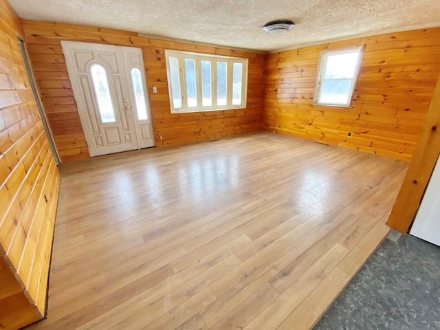 entrance foyer with a textured ceiling, wooden walls, and light hardwood / wood-style flooring