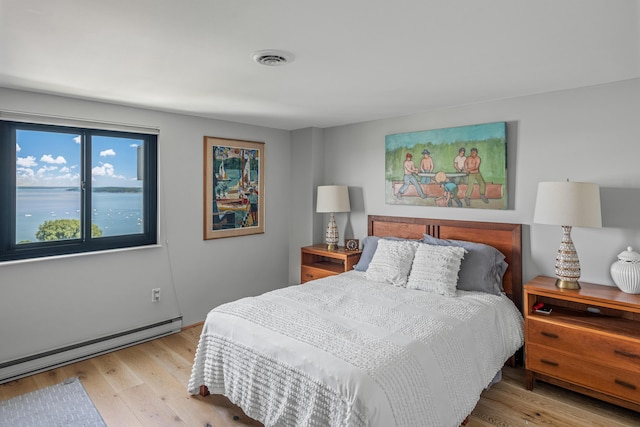 bedroom featuring light wood-type flooring, baseboard heating, and a water view