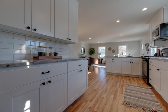 kitchen featuring white cabinetry, decorative backsplash, black range with gas stovetop, and kitchen peninsula