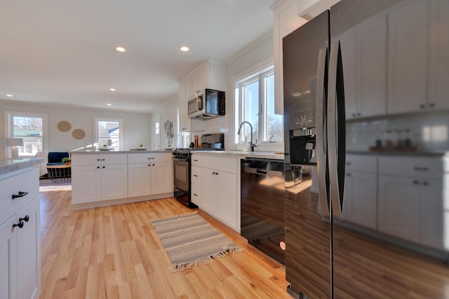 kitchen featuring sink, white cabinets, light hardwood / wood-style floors, kitchen peninsula, and black appliances