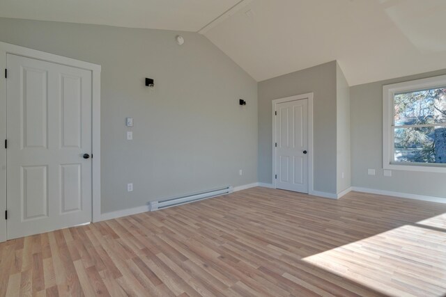 empty room featuring lofted ceiling, baseboard heating, and light wood-type flooring