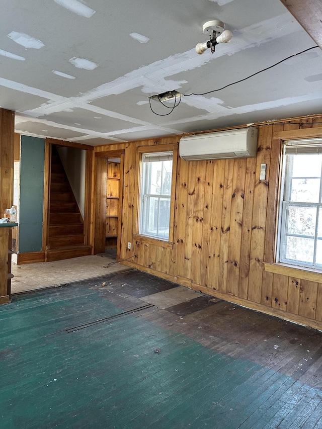 spare room with dark hardwood / wood-style flooring, wooden walls, a wall mounted AC, and plenty of natural light