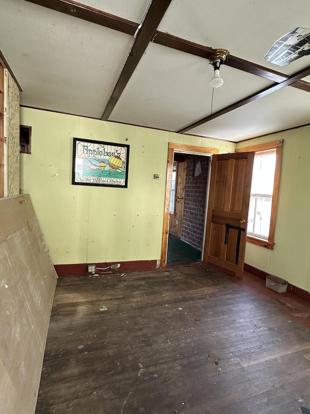 empty room featuring dark wood-type flooring, wooden walls, and beamed ceiling