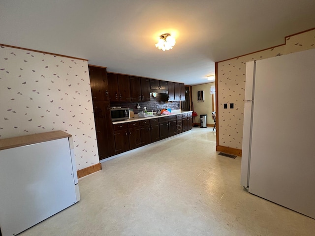 kitchen with white refrigerator, dark brown cabinets, and tasteful backsplash