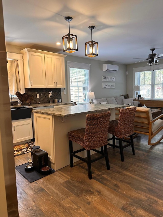 kitchen with decorative light fixtures, tasteful backsplash, an AC wall unit, dark wood-type flooring, and white cabinets