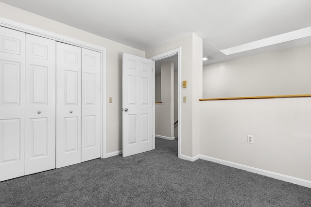 unfurnished bedroom featuring a skylight, a closet, and dark colored carpet