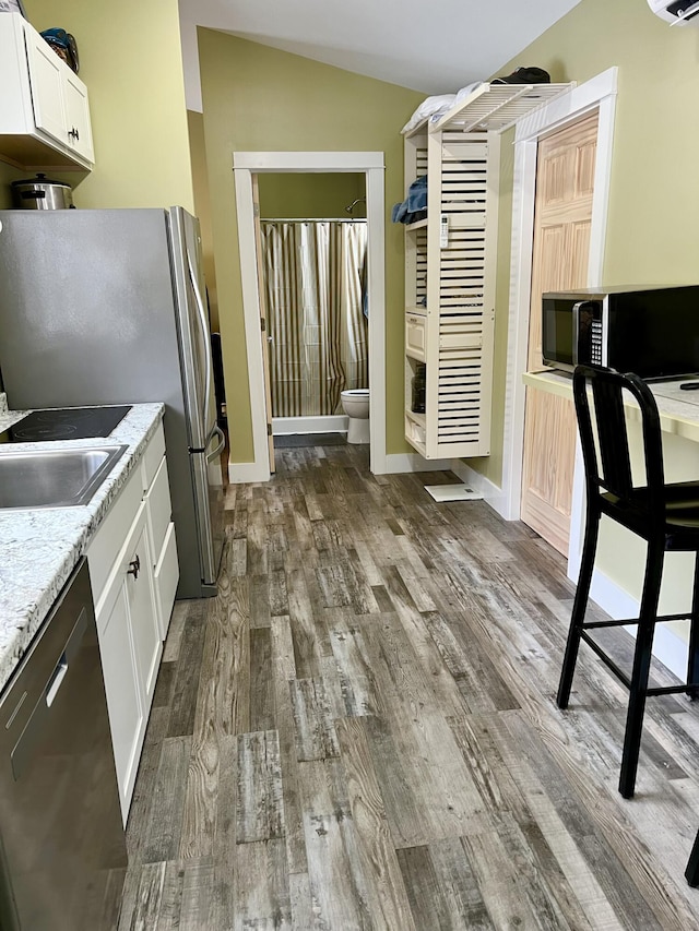 kitchen with stainless steel appliances, dark wood-type flooring, lofted ceiling, light stone countertops, and white cabinets