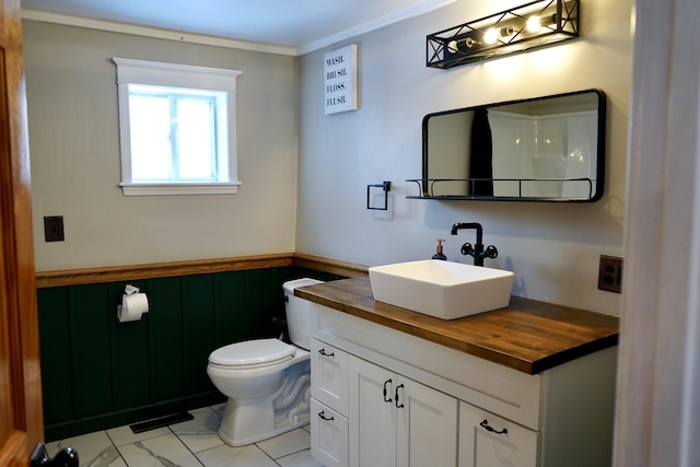 bathroom featuring toilet, vanity, wooden walls, and ornamental molding