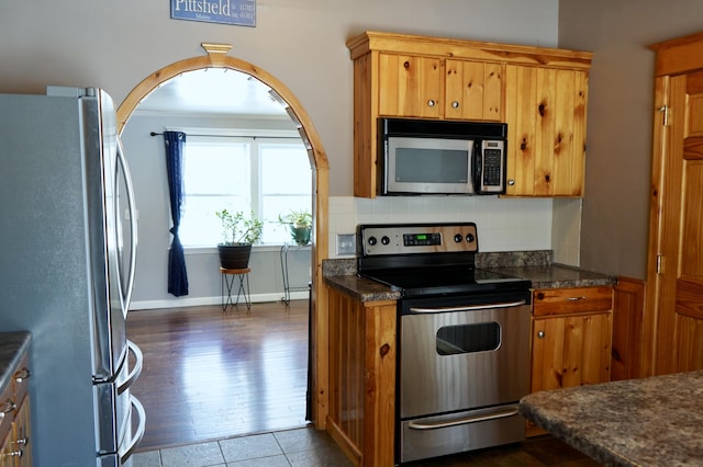 kitchen featuring appliances with stainless steel finishes, decorative backsplash, dark stone countertops, and dark tile patterned floors