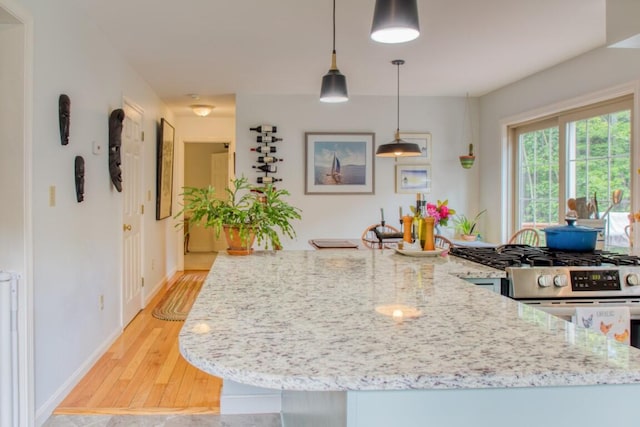 kitchen with stainless steel gas range oven, light hardwood / wood-style flooring, light stone countertops, and pendant lighting