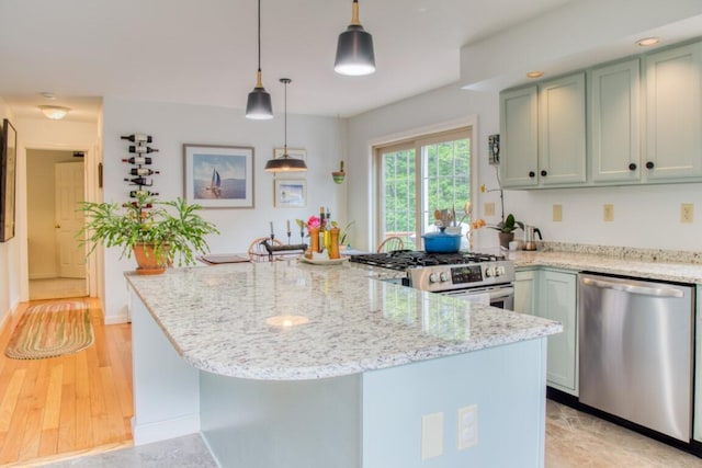 kitchen featuring kitchen peninsula, green cabinets, hanging light fixtures, appliances with stainless steel finishes, and light stone counters