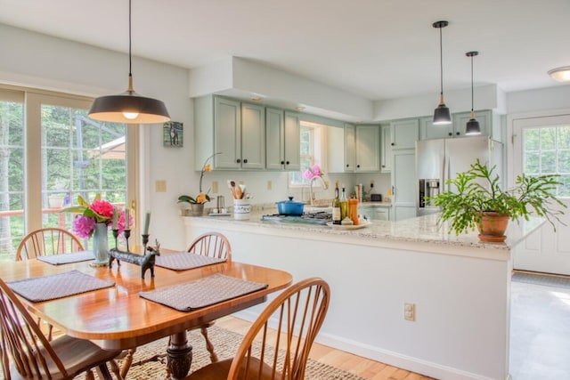 kitchen with stainless steel refrigerator with ice dispenser, kitchen peninsula, hanging light fixtures, and light stone countertops