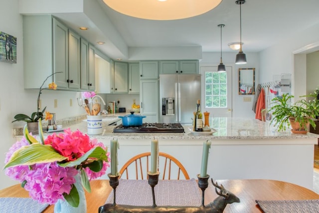 kitchen featuring decorative light fixtures, kitchen peninsula, light stone countertops, appliances with stainless steel finishes, and green cabinetry