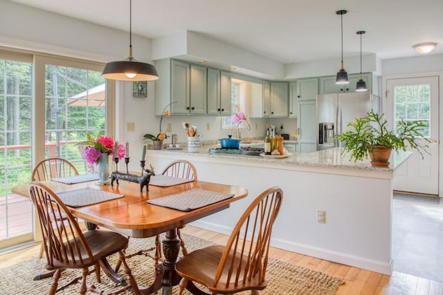 kitchen with kitchen peninsula, stainless steel fridge with ice dispenser, light stone counters, and green cabinets