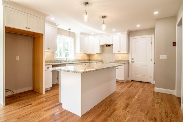 kitchen with light stone countertops, pendant lighting, a center island, white cabinetry, and light hardwood / wood-style floors