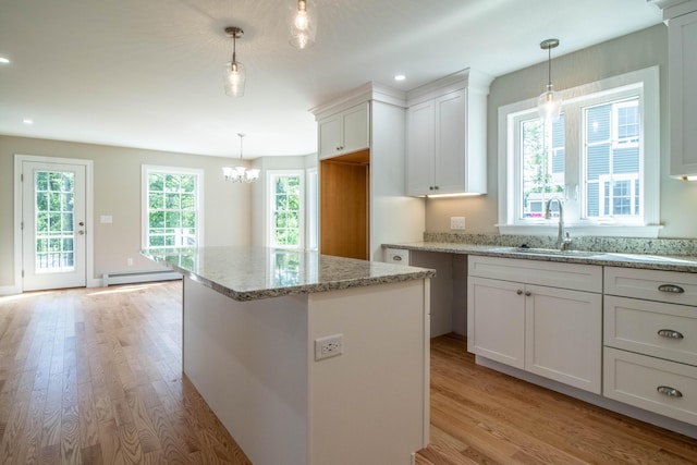 kitchen featuring baseboard heating, white cabinets, a kitchen island, decorative light fixtures, and light hardwood / wood-style flooring