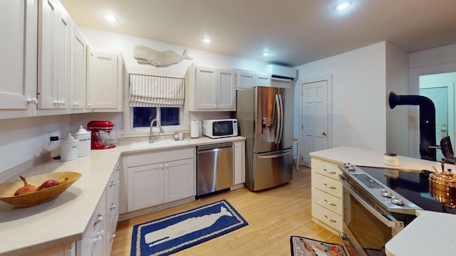 kitchen with light hardwood / wood-style floors, white cabinetry, an AC wall unit, sink, and stainless steel appliances