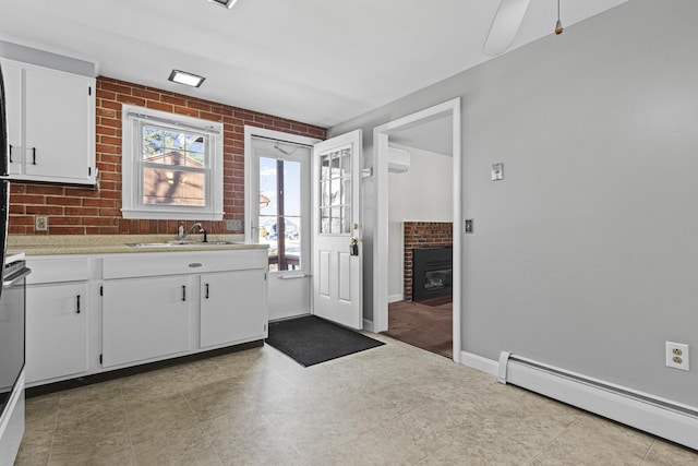 kitchen featuring an AC wall unit, sink, white cabinets, brick wall, and a baseboard radiator