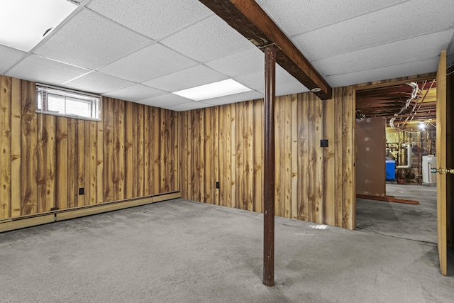 basement featuring carpet, a baseboard heating unit, wood walls, a drop ceiling, and gas water heater