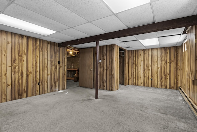 basement featuring carpet floors, a paneled ceiling, wood walls, and a baseboard radiator