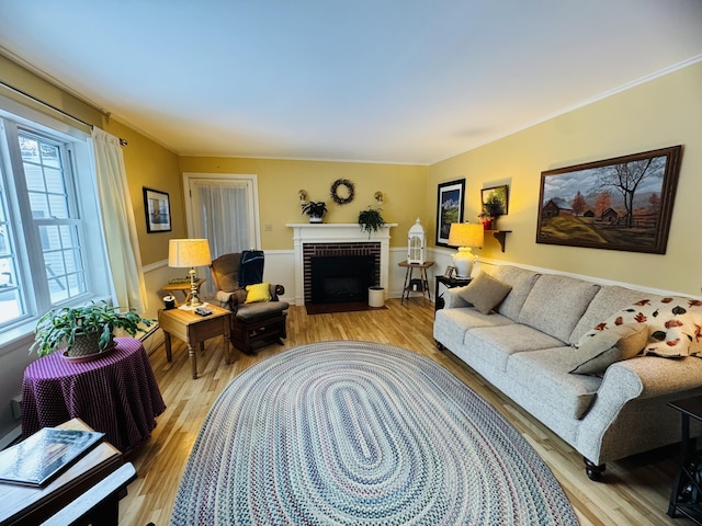 living room with light wood-type flooring, a brick fireplace, and ornamental molding