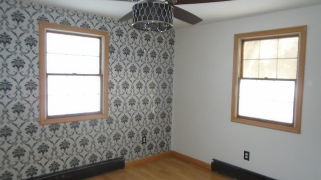 unfurnished room with a baseboard radiator, hardwood / wood-style floors, and a healthy amount of sunlight