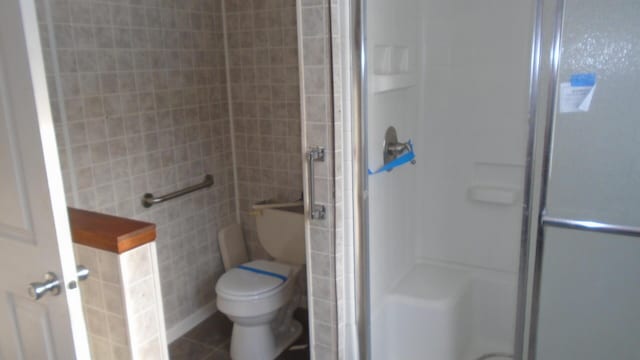 bathroom with toilet, a shower with door, and tile patterned flooring