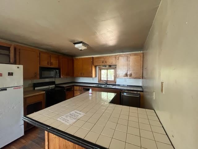 98 White Schoolhouse Rd, Corinth, ME 04427 - kitchen with a sink, brown cabinetry, black appliances, dark wood finished floors, and tile counters