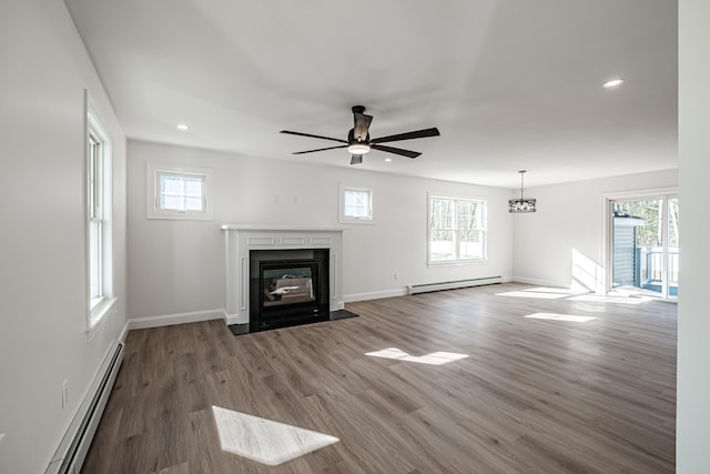 unfurnished living room with ceiling fan, a baseboard radiator, hardwood / wood-style floors, and a healthy amount of sunlight