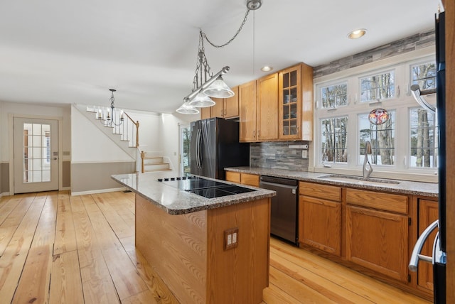 kitchen featuring sink, light wood-type flooring, a center island, black appliances, and decorative backsplash