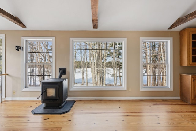 unfurnished dining area featuring light hardwood / wood-style floors, a wood stove, and beam ceiling