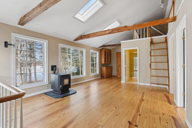 unfurnished living room with light hardwood / wood-style floors, vaulted ceiling with skylight, a wealth of natural light, and a wood stove