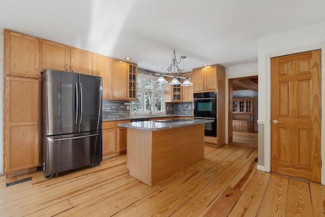 kitchen featuring black appliances, a center island, decorative light fixtures, backsplash, and light wood-type flooring