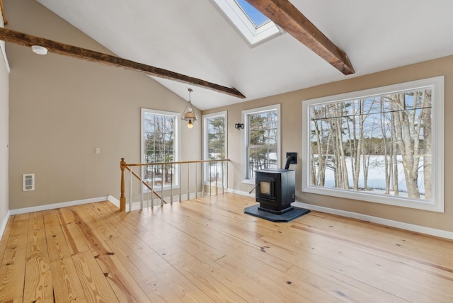 unfurnished living room with light hardwood / wood-style floors, a wood stove, and vaulted ceiling with skylight