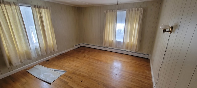 unfurnished room with baseboard heating, hardwood / wood-style flooring, and wooden walls