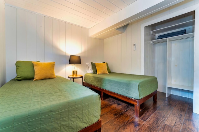 bedroom with a closet, dark hardwood / wood-style flooring, and wooden walls