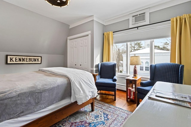 bedroom featuring a wall mounted air conditioner, wood-type flooring, a closet, and baseboard heating